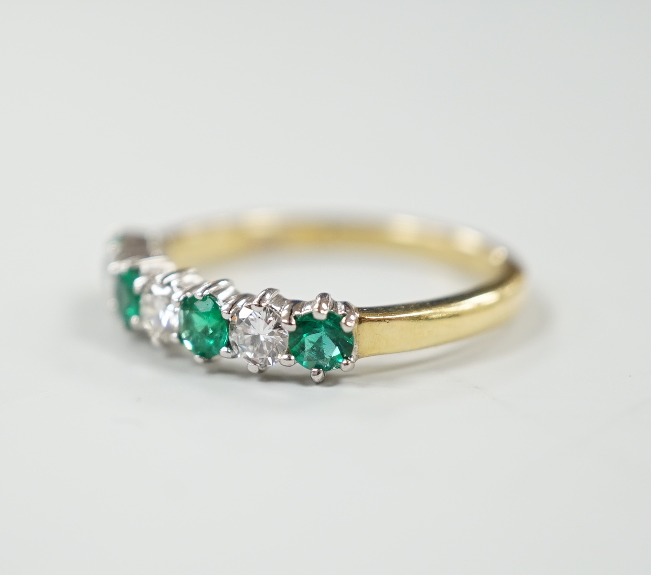 A modern 18ct gold, four stone emerald and three stone diamond set half hoop ring, size M, gross weight 2.9 grams.
